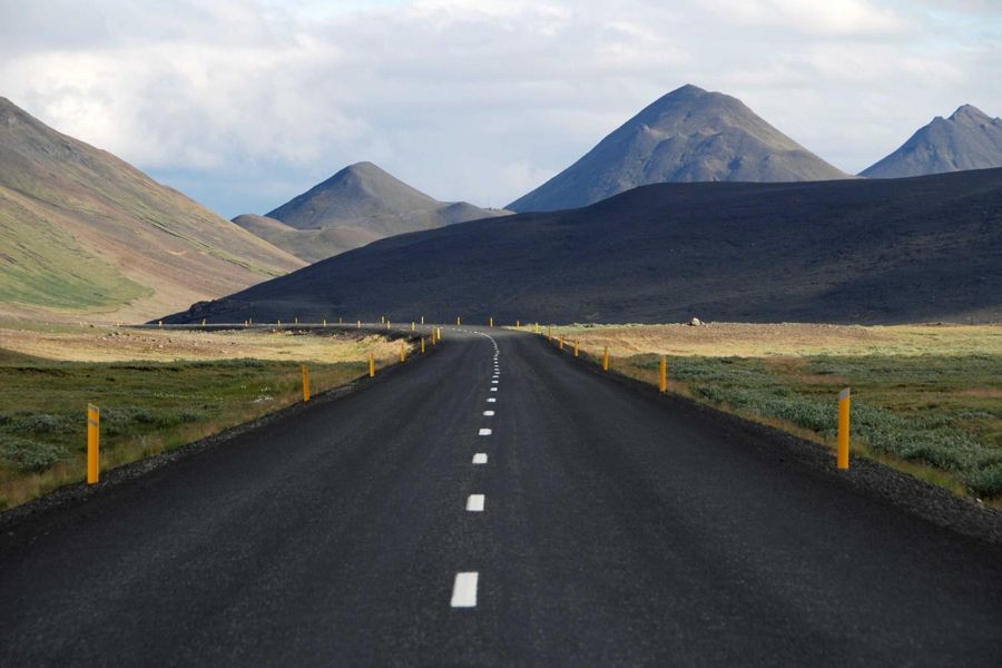 Two-lane asphalt road with yellow edge posts running toward dark mountains