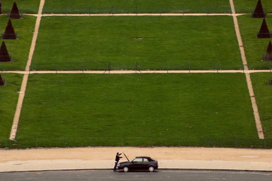 Large terraced lawns with gravel paths, seen from above, and a small car on the road below